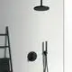 Schwarze Dusche von Ideal Standard, bestehend aus einer runden Regendusche, Handbrause und Steuerung, montiert an einer hellen Wand. Handtuchhalter sowie Handtuch sichtbar.